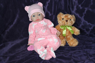 A baby doll holding a pacifier is placed next to a plush teddy bear on a neutral background.